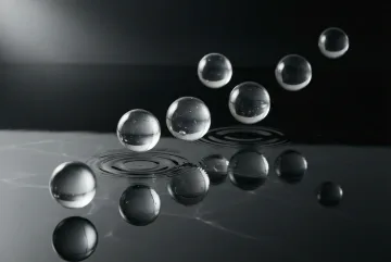 Seven translucent glass orbs suspended above rippling black water with silver reflections in a minimalist fine art photographic composition.
