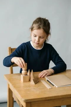 Young student arranging wooden geometric solids on a learning desk during a hands-on spatial reasoning activity.