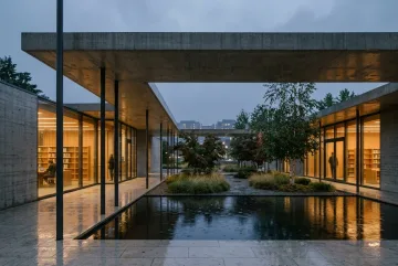 Cinematic modern public library with a cantilevered concrete roof surrounding a rain-soaked courtyard and reflecting pool illuminated by warm reading-room lights.