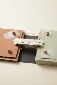 Kolase Mixed Media berupa jembatan dari potongan kertas gading yang menghubungkan platform karton terakota dan hijau sage di atas celah gelap, dilengkapi cakram kertas, benang oker, dan lapisan vellum transparan.