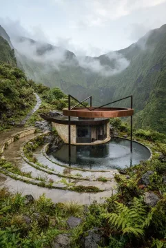 Photorealistic atmospheric observatory inside a misty green mountain crater, featuring a suspended copper condensation ring above a circular rainwater basin, curved limestone terraces, and wet stone pathways.