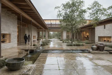 Landscape view of a contemporary community water archive pavilion surrounding a rain-cooled courtyard with pale masonry, timber galleries, reflective channels, native planting, and two anonymous visitors.