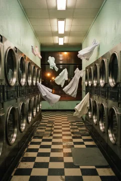 Surreal retro midnight laundromat with pastel clothes floating above chrome washing machines and a black-and-cream checkerboard floor.