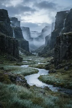 Cinematic misty basalt valley with a winding river, dark volcanic cliffs, silver grass, and soft dawn light in a vertical landscape.
